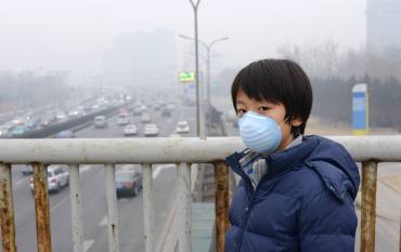 Child wears mouth mask in Beijing with air pollution in background.