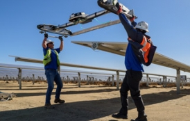 Workers at a solar station in the Mojave Desert attach a robot to clean panels.